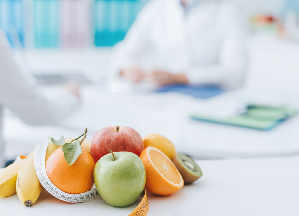Nutritionist meeting a patient in the office Professional nutritionist meeting a patient in the office and healthy fruits with tape measure on the foreground: healthy eating and diet concept
